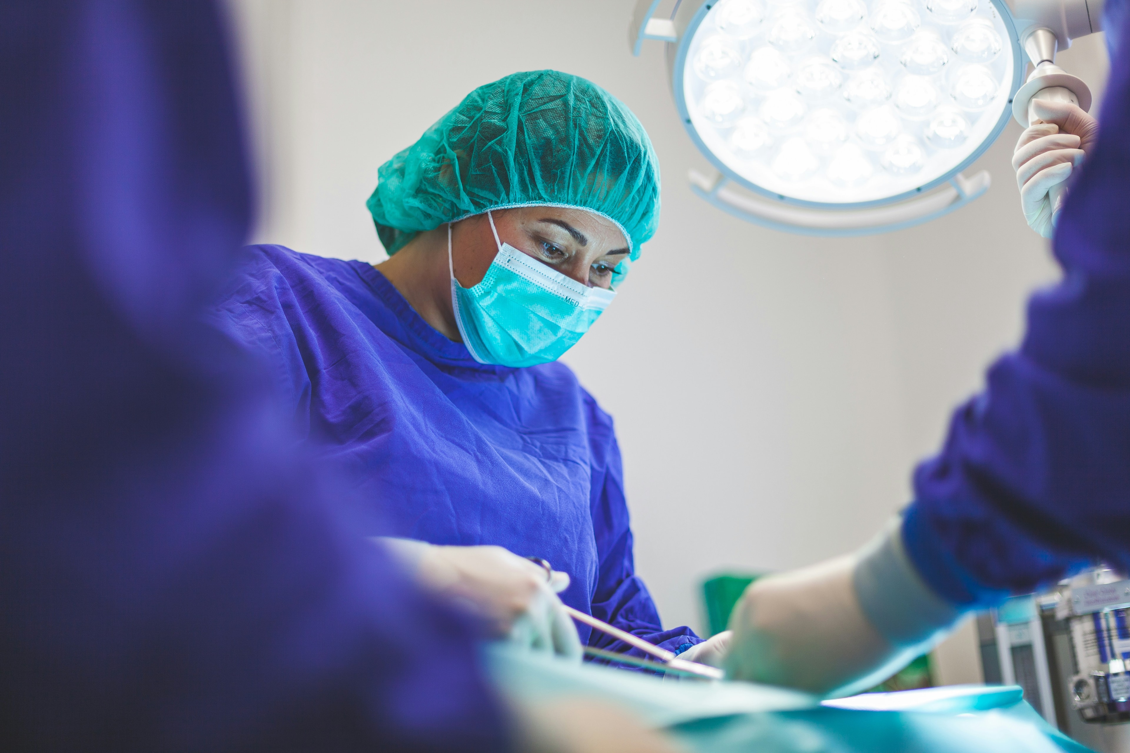 A veterinary team in blue scrubs working under a surgical light.